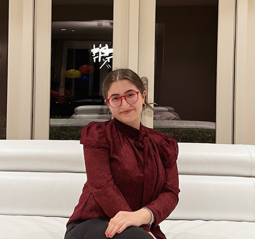 Photo of Romina, a woman with dark hair and red glasses wearing a red shirt and smiling with her mouth closed